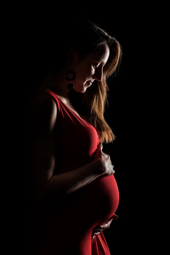 Di profilo, in abito rosso, una donna in gravidanza guarda la pancia