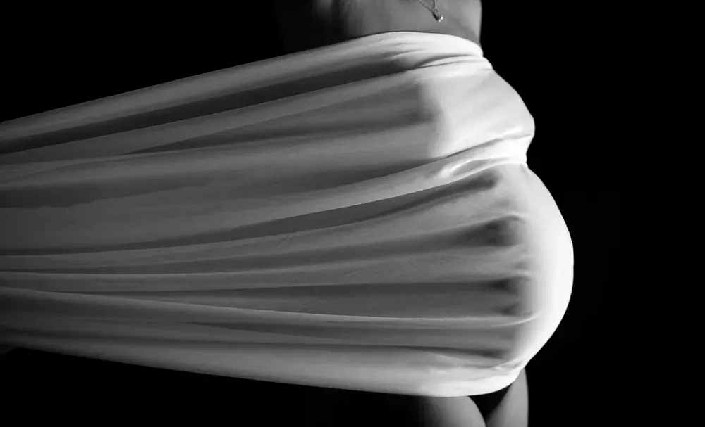 Pancia di una donna in gravidanza avvolta da un telo bianco teso, in bianco e nero