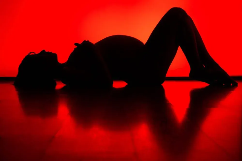 Donna in gravidanza distesa, in sagoma su fondo rosso, col riflesso sul pavimento