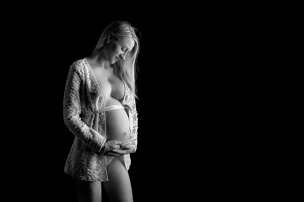 Ritratto in gravidanza in bianco e nero: donna bionda con una giacca di pizzo aperta e legata in vita