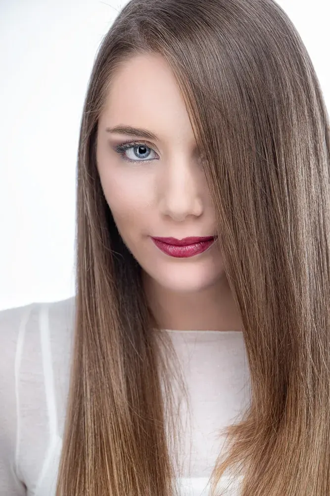 Primo piano di donna col rossetto scuro e i lunghi capelli castani che le coprono un occhio