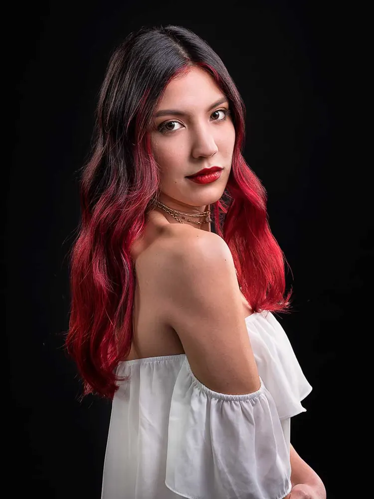 Donna coi capelli neri sfumati di rosso e un top bianco a spalle scoperte, che si volta verso l'obiettivo