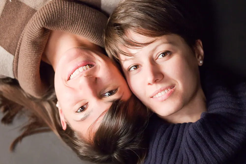 Due donne sdraiate, una a testa in giù rispetto all'altra, sorridono guardando l'obiettivo