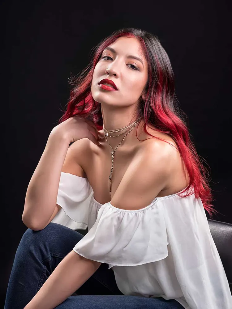 Donna seduta, con le punte dei capelli rosse e una camicetta bianca a spalle scoperte