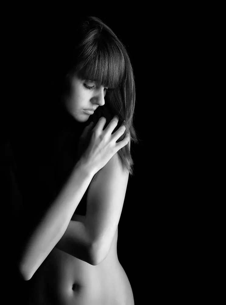 Donna con la frangia, a capo chino, col braccio sul petto e la mano sulla spalla, in bianco e nero