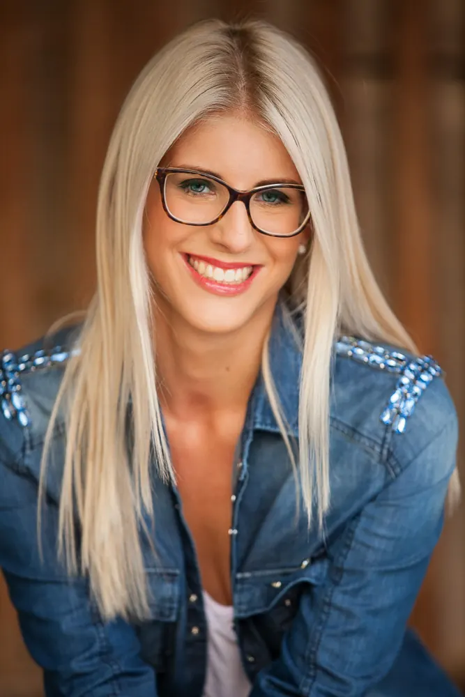 Ragazza bionda con occhiali e giacca di jeans con borchie sulle spalle, sorride guardando l'obiettivo