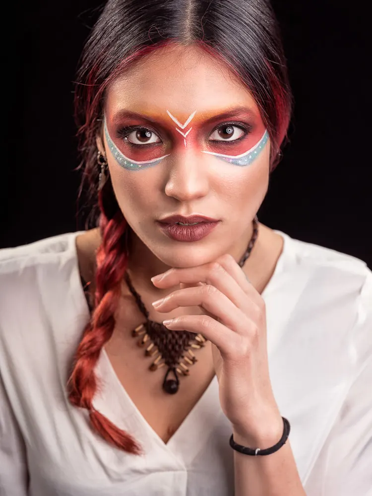 Donna con la mano sotto il mento, il trucco colorato intorno agli occhi e una treccia rossa