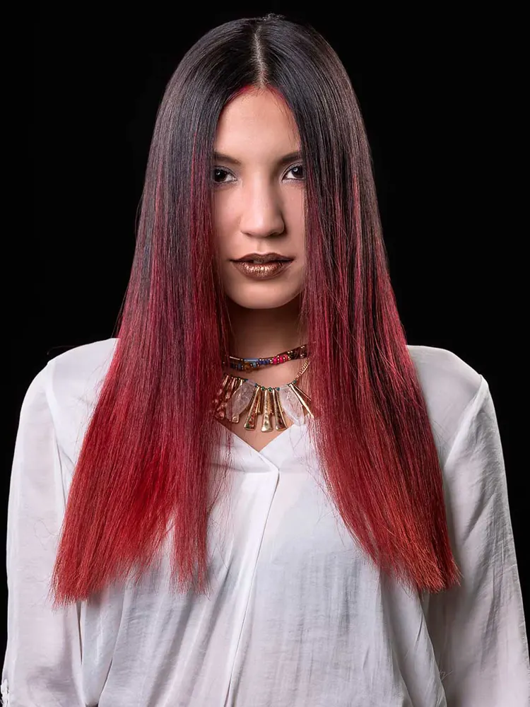 Donna di fronte all'obiettivo, coi capelli lisci neri e rossi, blusa bianca e collana dorata