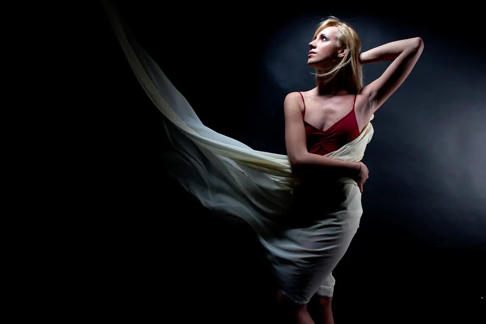 Ballerina bionda con un velo bianco mosso dal vento, top rosso e un braccio dietro la testa