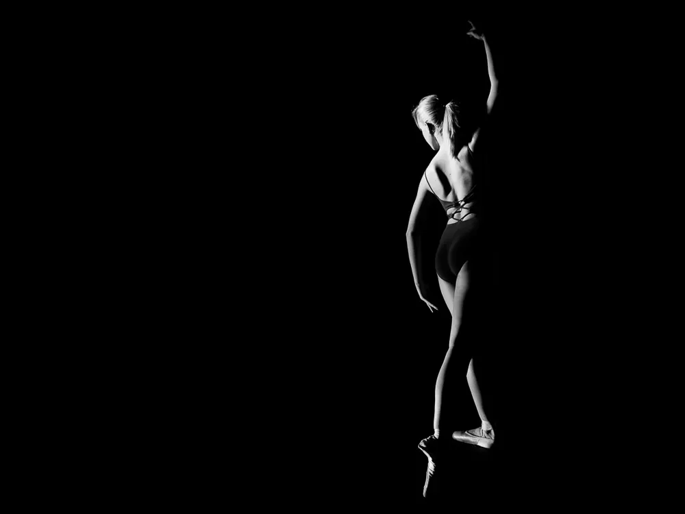 Ballerina vista di schiena, in punta di piedi con un braccio alzato, in bianco e nero