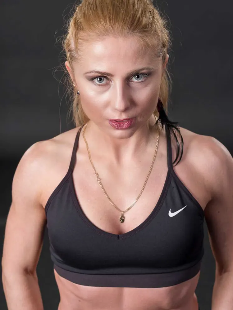 Ritratto ravvicinato di donna bionda con coda di cavallo e reggiseno sportivo nero, sguardo diretto