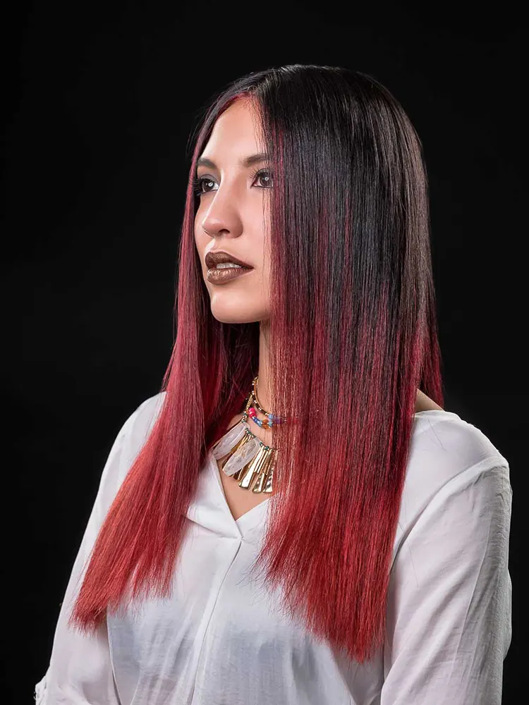 Donna di profilo con lunghi capelli neri e rossi, camicia bianca e collana di piume