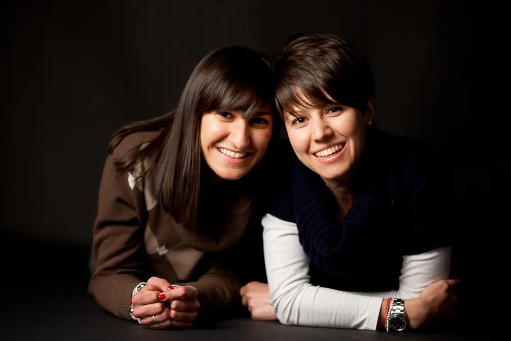 Due donne sdraiate sul ventre che sorridono, una in maglione marrone e l'altra in dolcevita blu