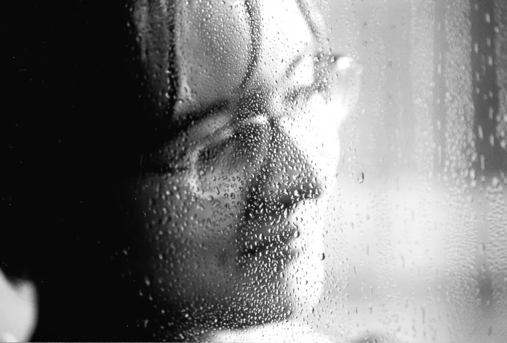 Volto di donna dietro un vetro rigato di gocce d'acqua, in bianco e nero