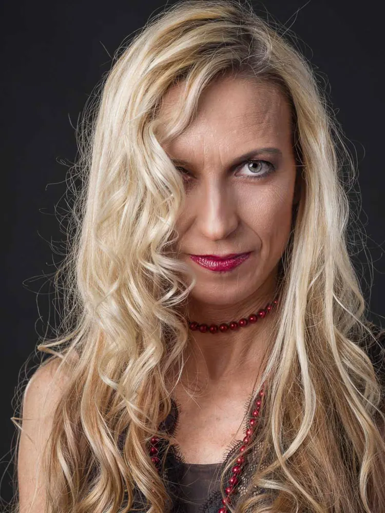 Donna con una collana di perline rosse e i lunghi capelli biondi ondulati su un occhio