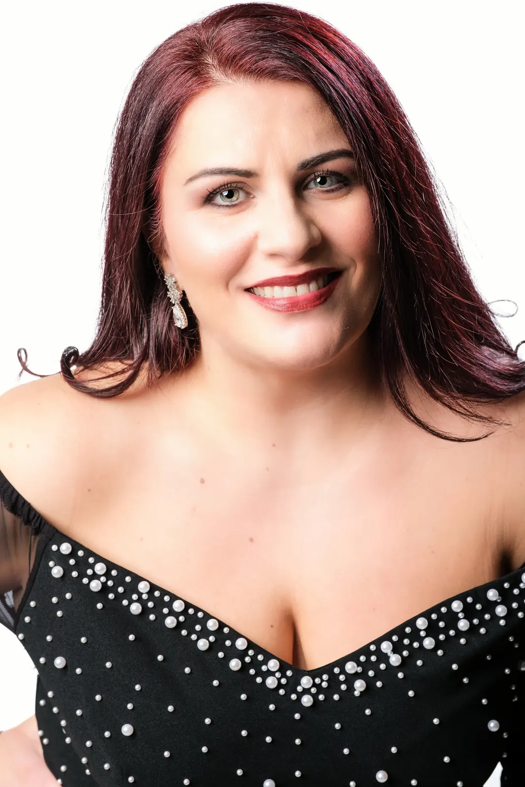 Cantante coi capelli bordeaux e un abito nero con perle, su fondo bianco