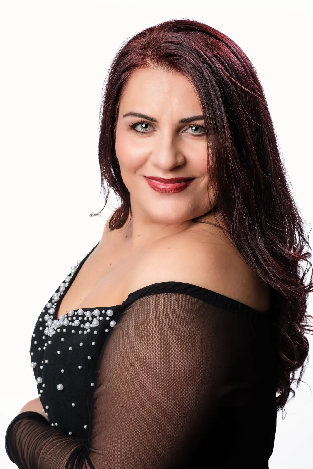 Primo piano di una cantante coi capelli bordeaux e l'abito nero con le perline, che sorride