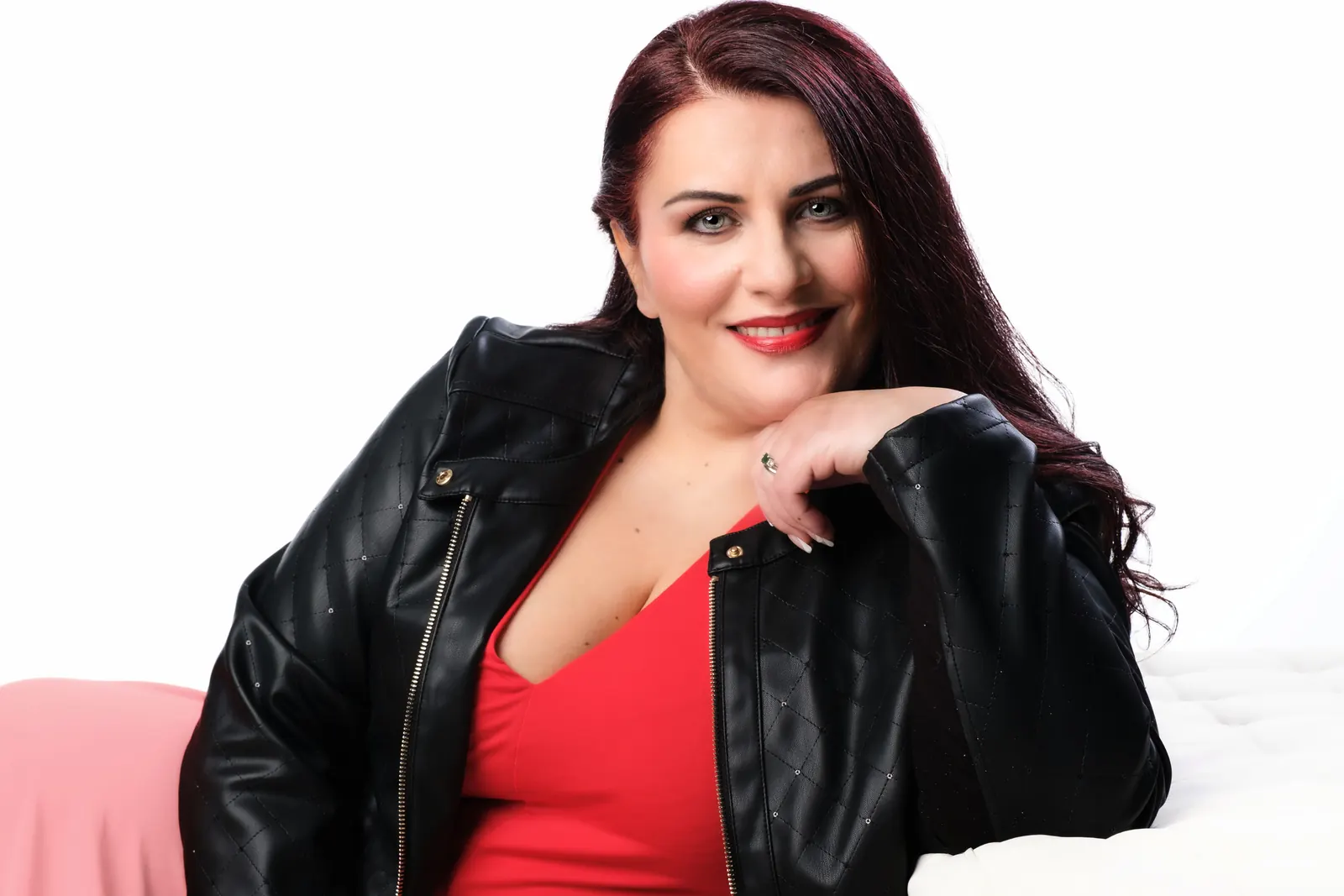 Cantante che sorride col mento appoggiato sulla mano, in giacca di pelle e top rosso