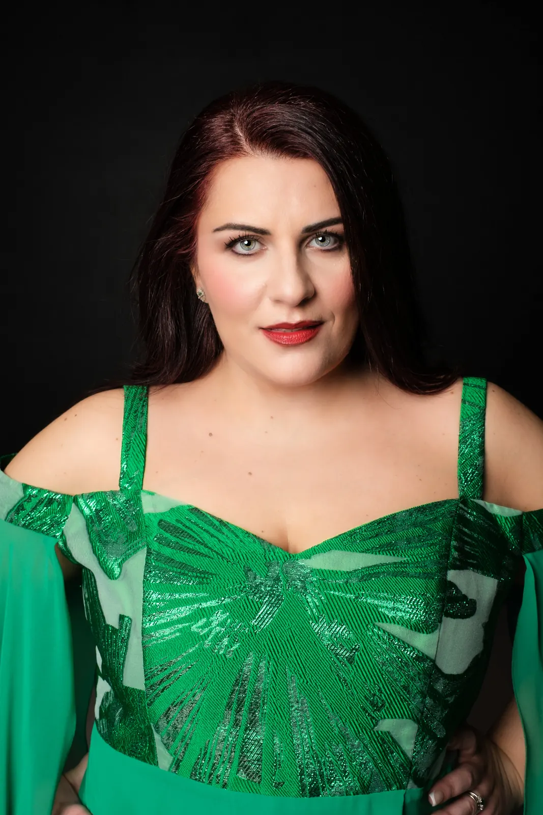 Primo piano di una cantante con il corpetto verde lucido e le labbra rosse, su fondo nero