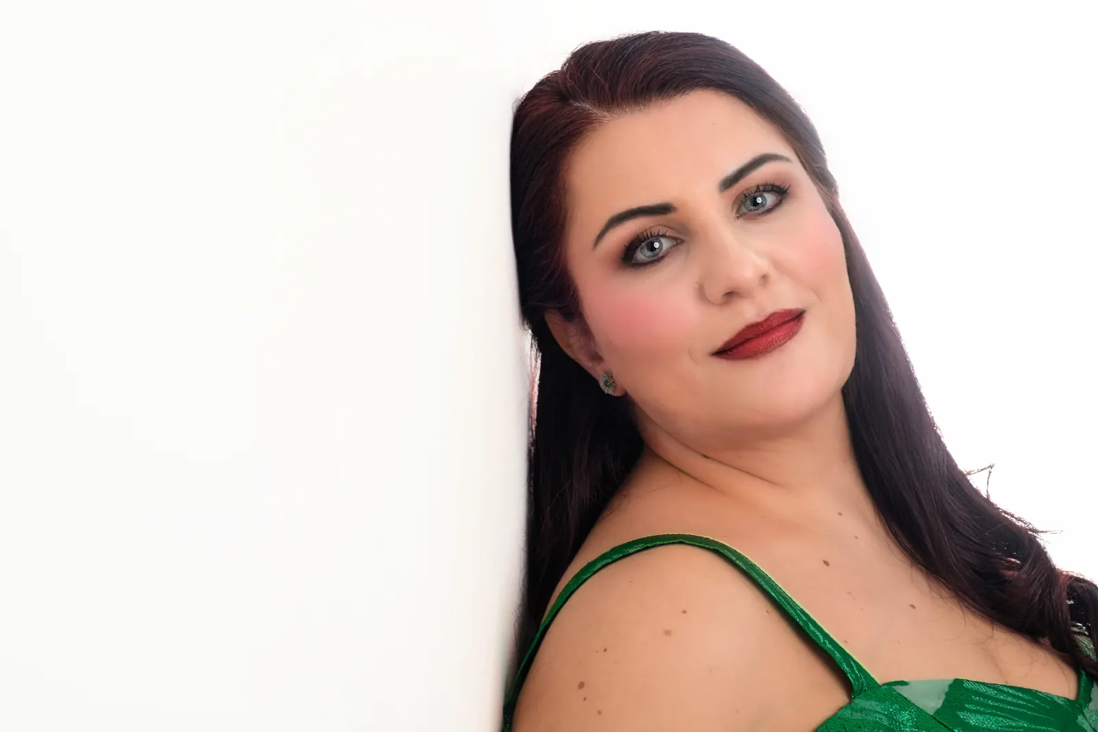Ritratto di una cantante con una spallina verde e le labbra rosso scuro, appoggiata al muro