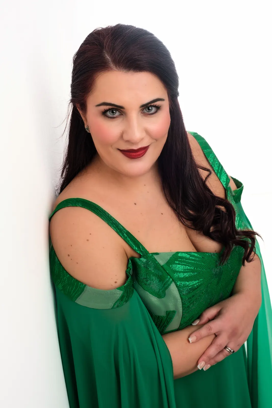 Cantante in abito verde appoggiata a una parete bianca, con le mani incrociate