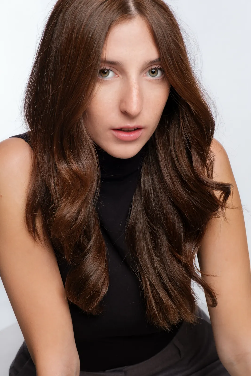 Ragazza coi capelli castani lunghi, china in avanti verso l'obiettivo, in dolcevita nero senza maniche