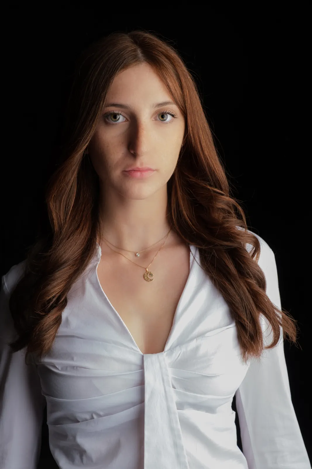 Ritratto di donna dai lunghi capelli castani mossi, camicia bianca e collana sottile, su fondo nero