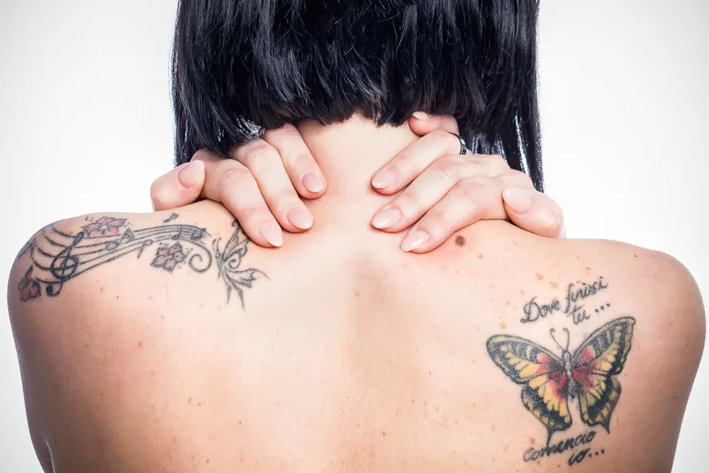 Donna di schiena con le mani sul collo e due tatuaggi: uno spartito e una farfalla