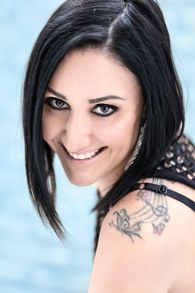 Cantante dai capelli neri che sorride guardando l'obiettivo, con un tatuaggio musicale sulla spalla