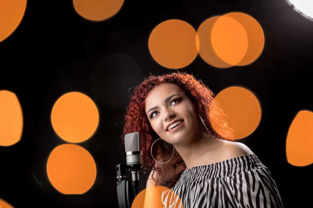 Cantante coi capelli rossi ricci davanti al microfono, con grandi cerchi arancioni di luce sullo sfondo