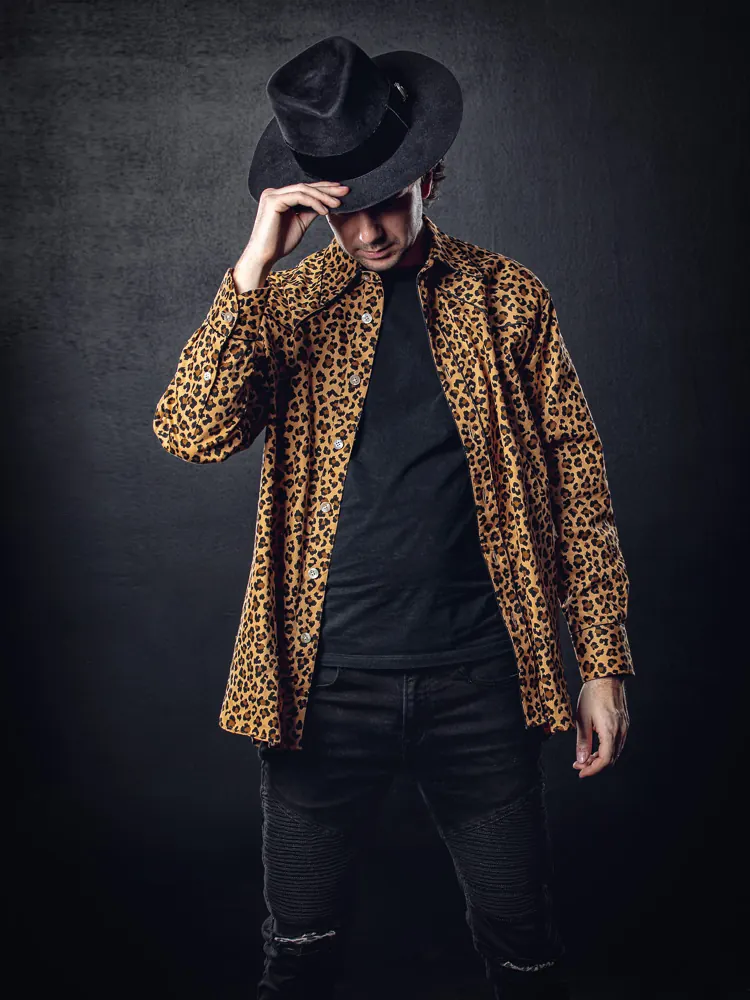 A testa china, un uomo in camicia leopardata tiene una mano sulla tesa del cappello nero