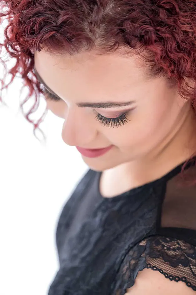 Ragazza coi ricci rossi vista dall'alto, con gli occhi bassi e un top nero di pizzo