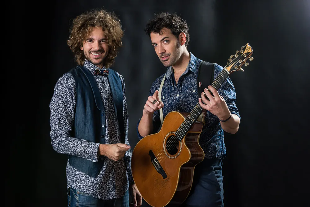 Due musicisti, uno col papillon e il gilet di jeans, l'altro con una chitarra acustica in mano