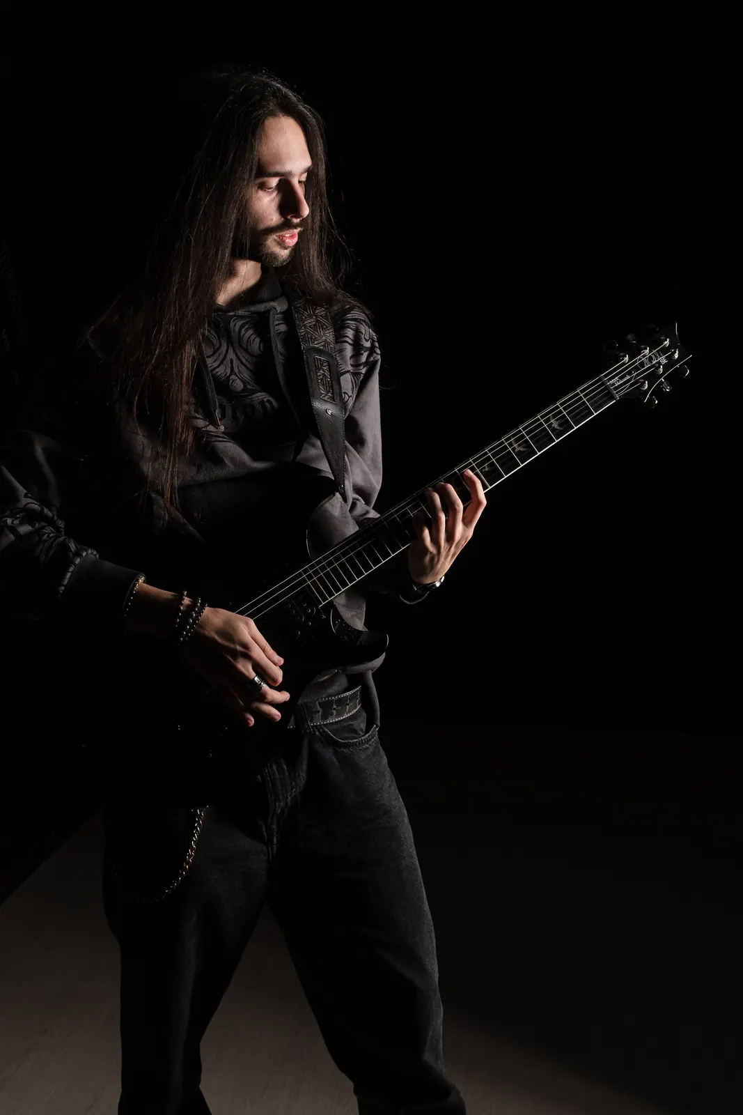Chitarrista coi capelli lunghi con lo sguardo sulla tastiera della chitarra nera
