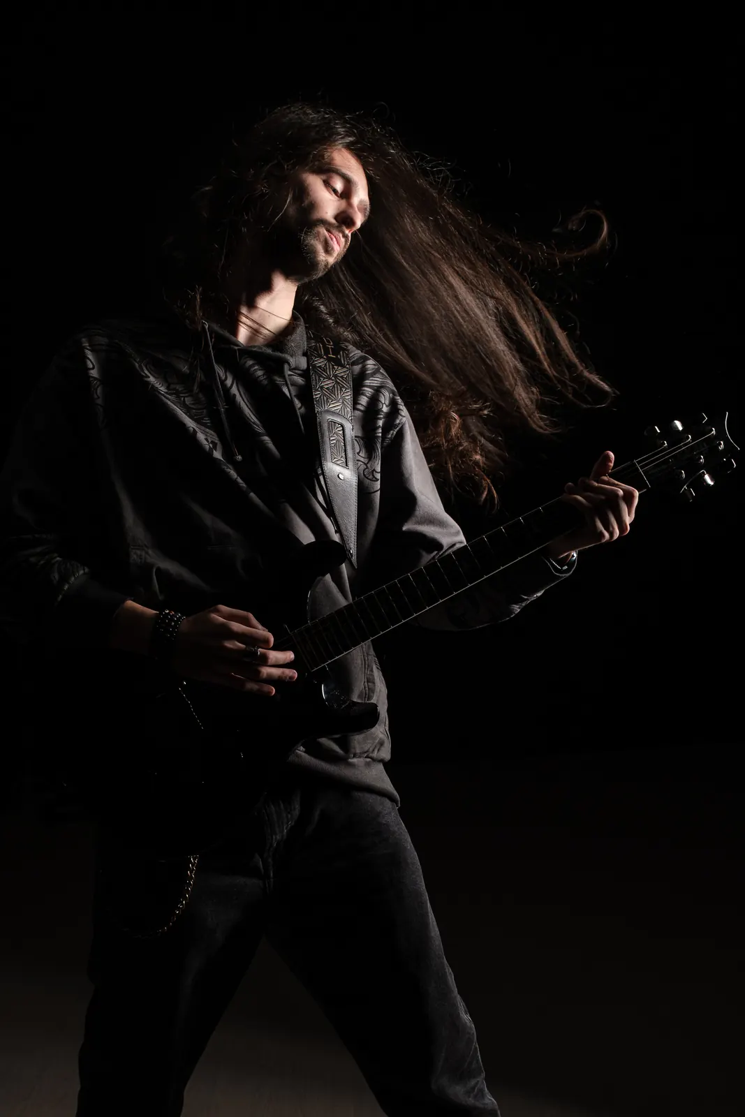 Chitarrista che suona la chitarra nera coi capelli lunghi in volo