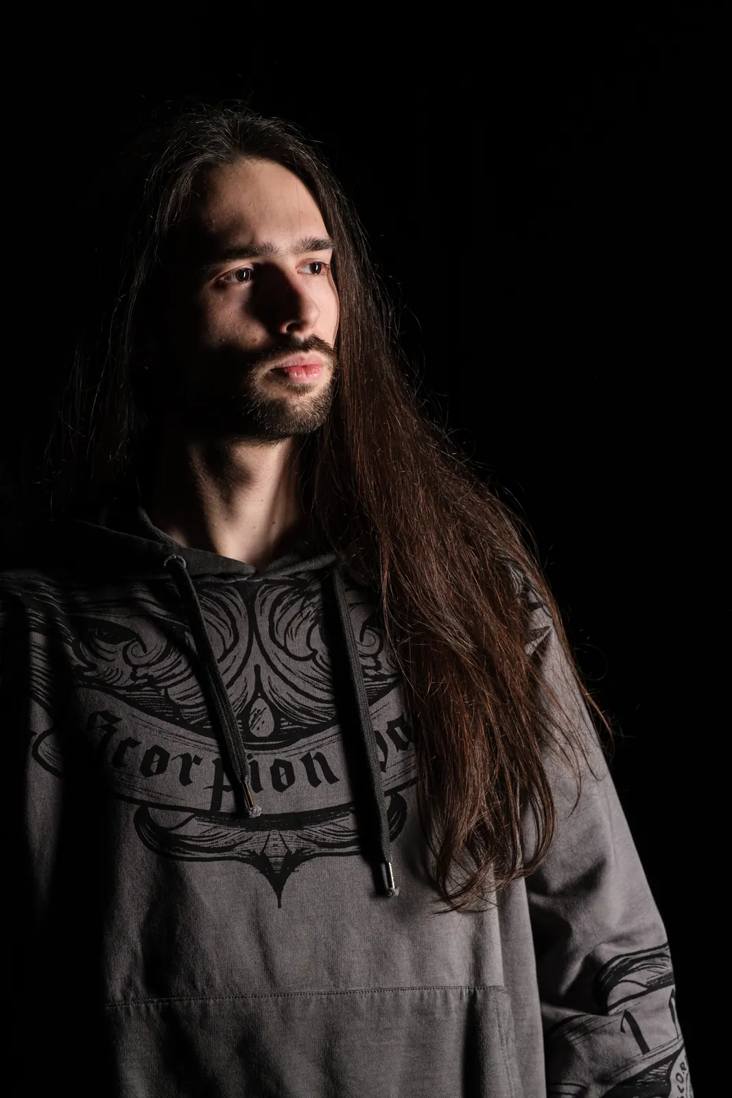 Ritratto di un ragazzo coi capelli lunghi e la felpa grigia, sguardo di lato