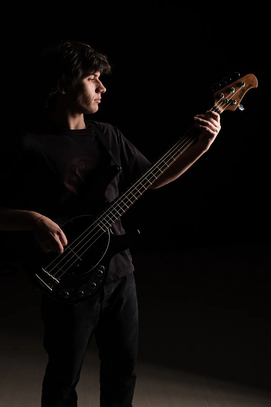 Bassista di profilo che guarda il manico del suo basso nero