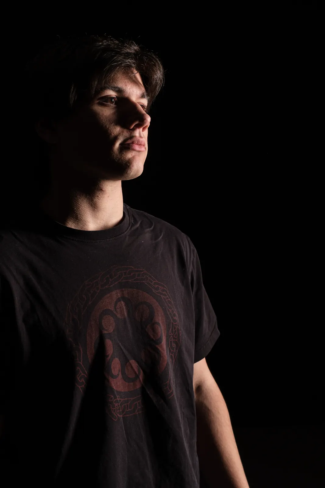 Ragazzo in maglietta nera con un disegno rosso, il viso in luce laterale su fondo nero