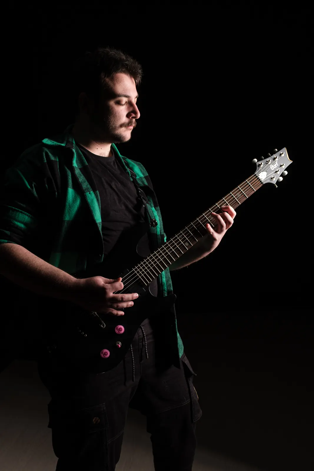 Chitarrista in camicia a quadri verde con gli occhi sulla tastiera della chitarra