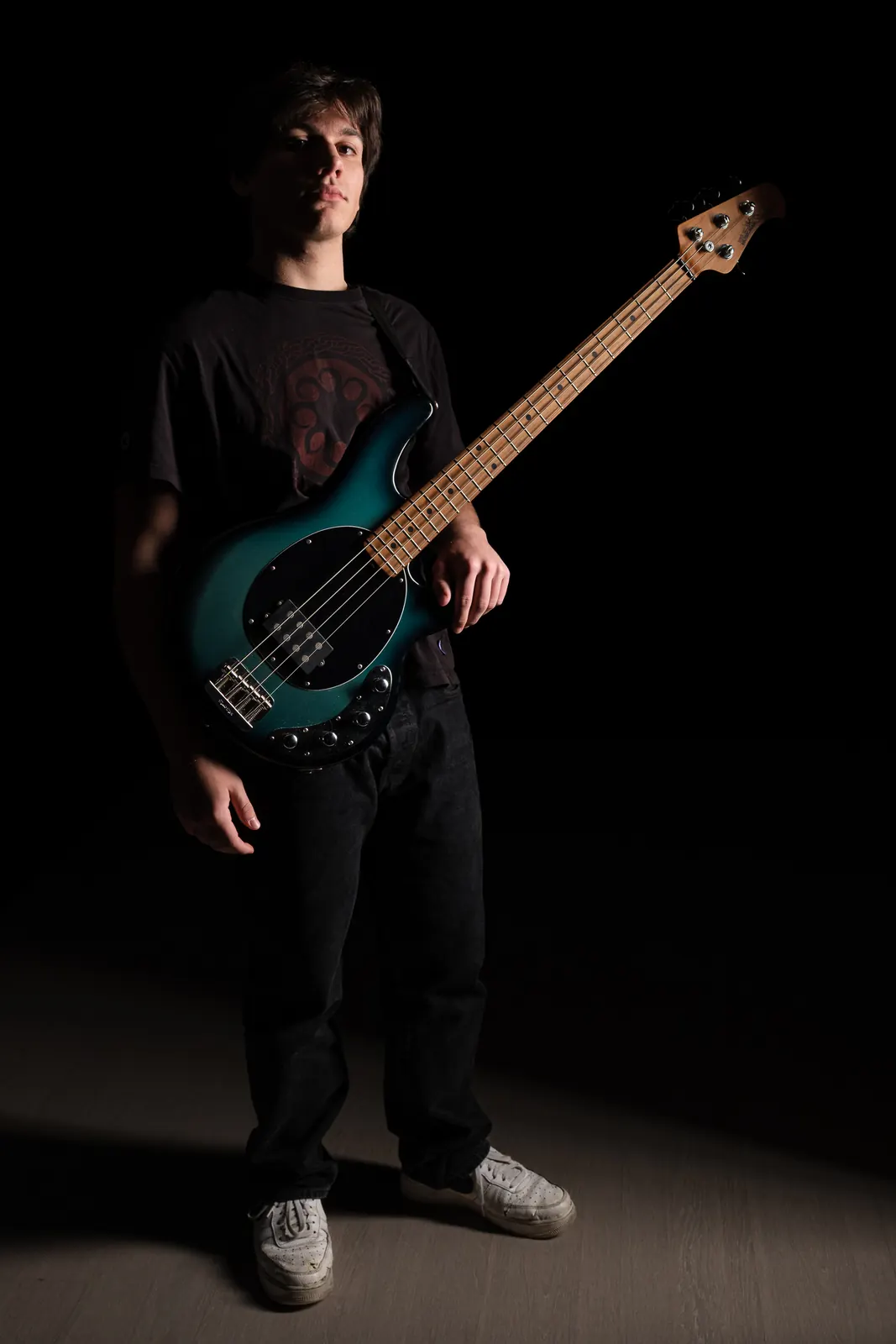 Bassista in piedi con un basso verde-blu, in luce laterale