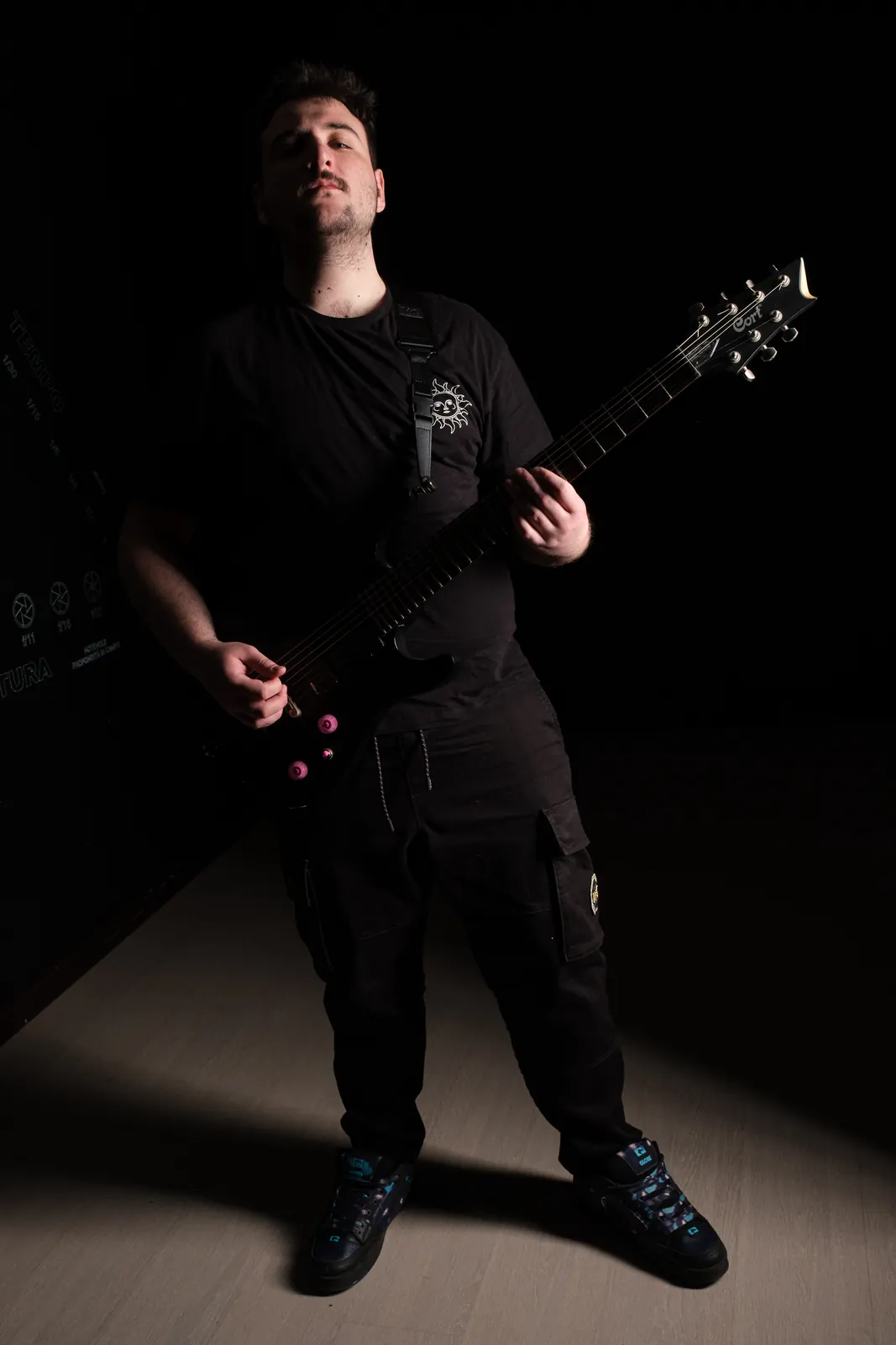 Chitarrista in piedi con la chitarra nera, un fascio di luce sul pavimento