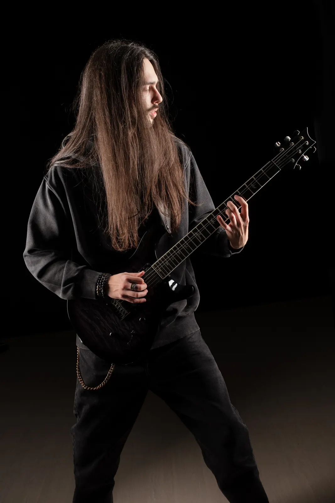 Chitarrista coi capelli lunghi e il viso girato di lato mentre suona la chitarra nera