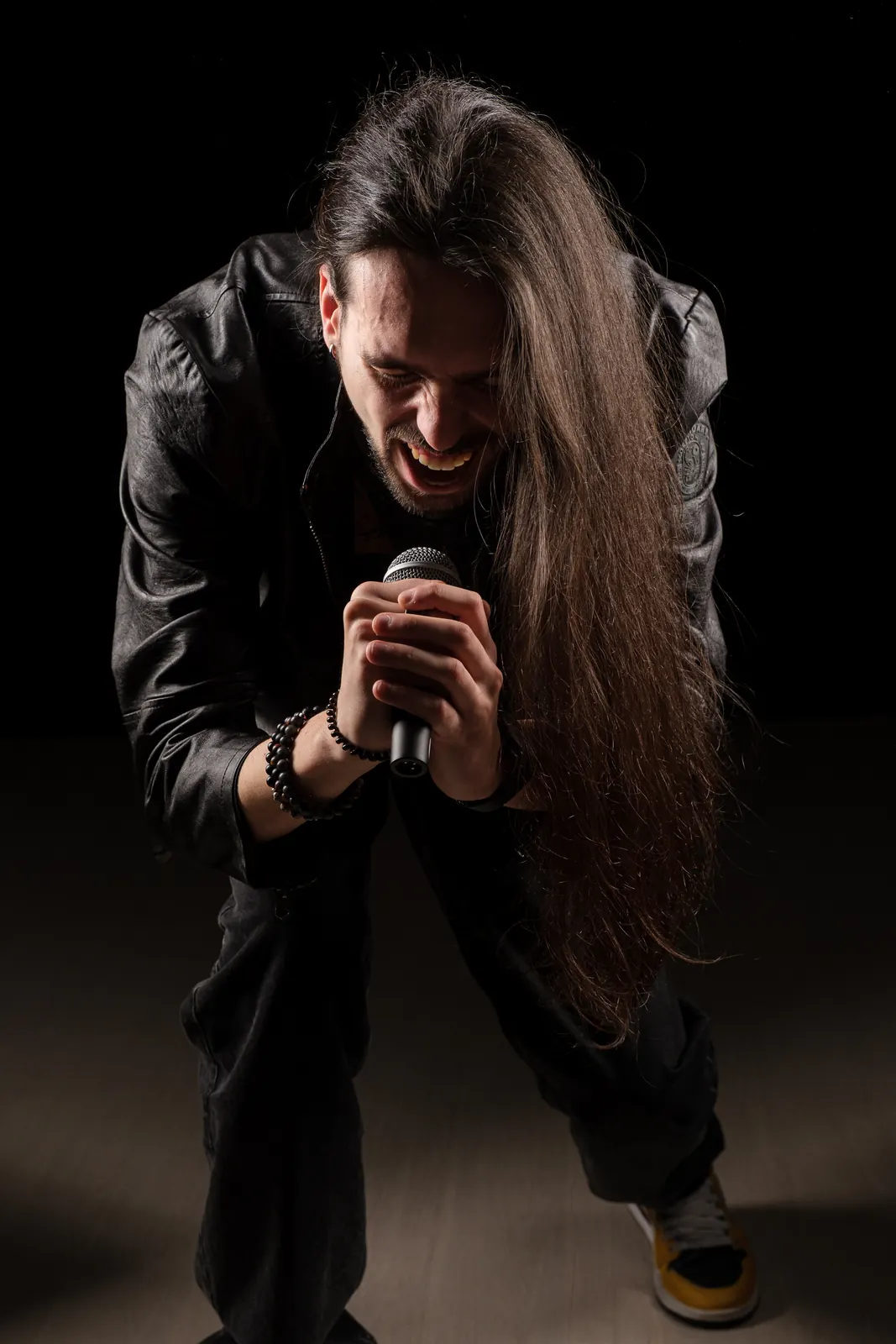 Cantante coi capelli lunghissimi, piegato in avanti con le mani strette attorno al microfono