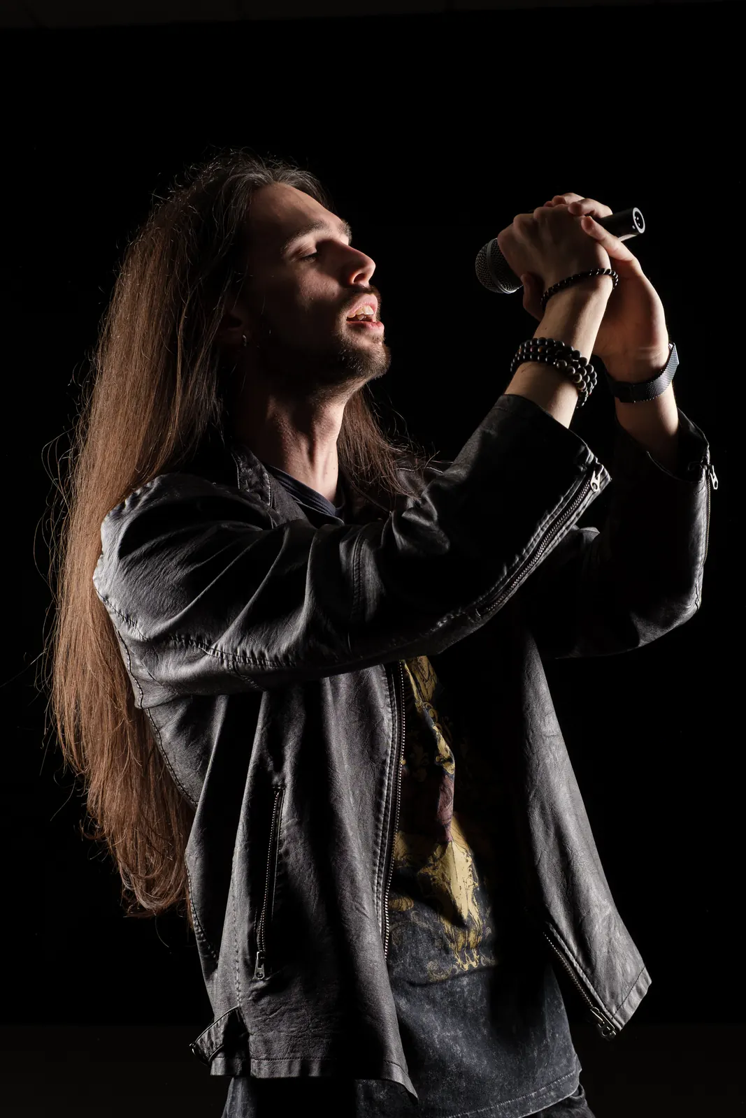 Cantante in giacca di pelle ripreso di profilo, con tutte e due le mani sul microfono