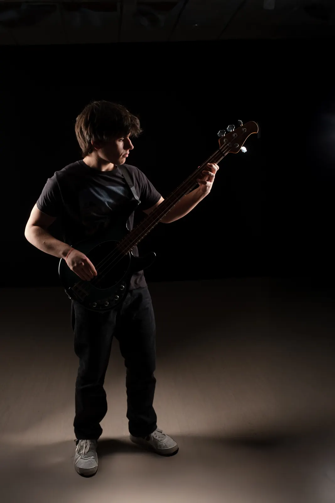 Bassista in piedi che guarda la tastiera, con la luce sul pavimento